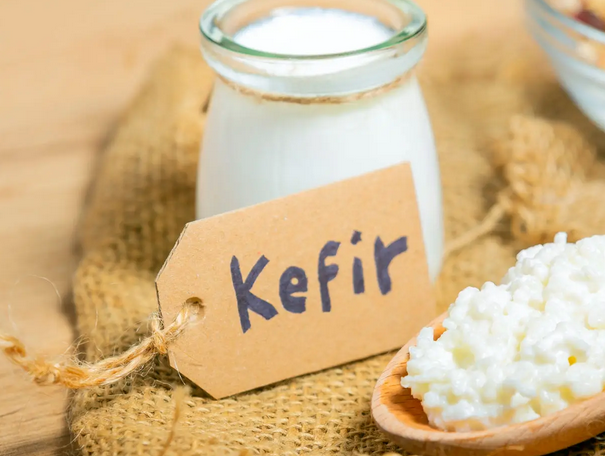 A jar of liquid kefir and a wooden spoon with kefir grains.