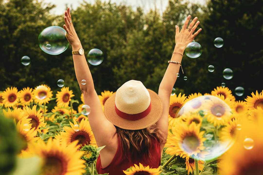 Woman in a sunflower field with arms raised toward bubbles.