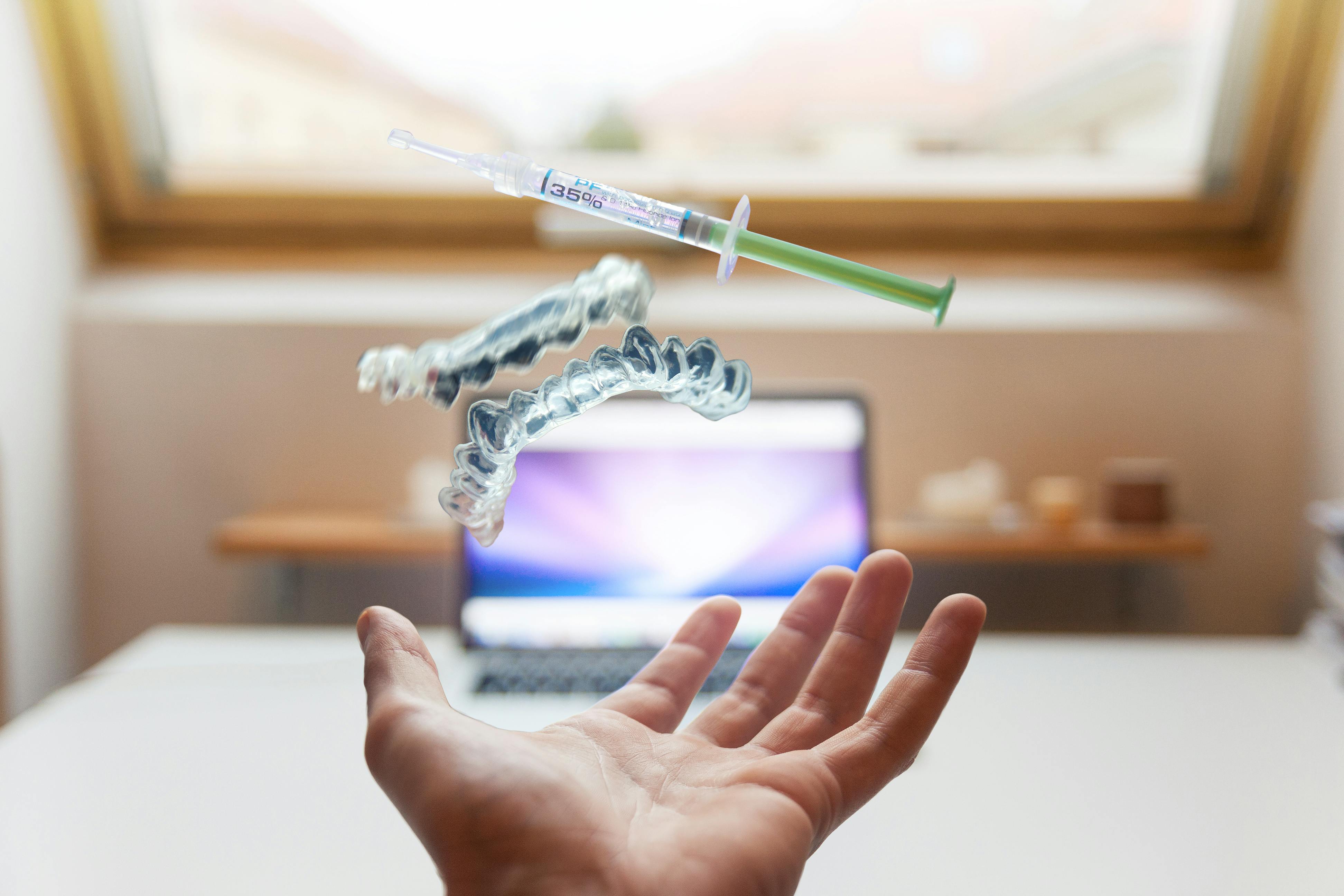 Dental aligners and a treatment syringe floating above an open hand.