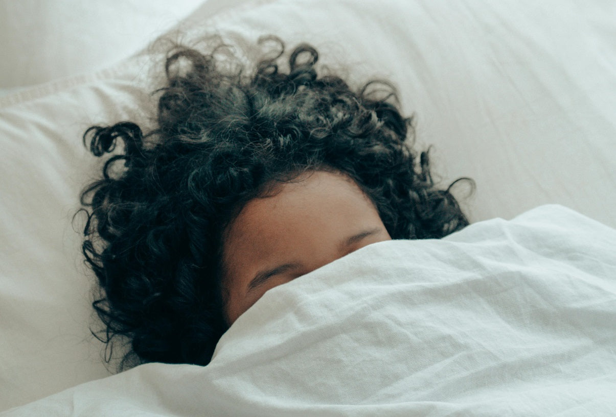 Person with curly hair tucked under a white blanket.
