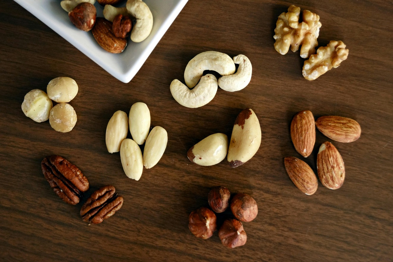 Various nuts including cashews, almonds, and walnuts spread on a wooden surface.