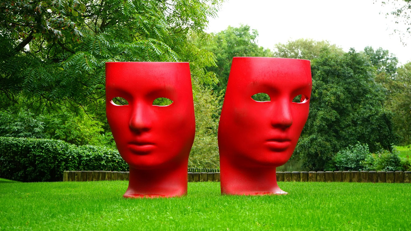 Two large red face sculptures standing on a green lawn.
