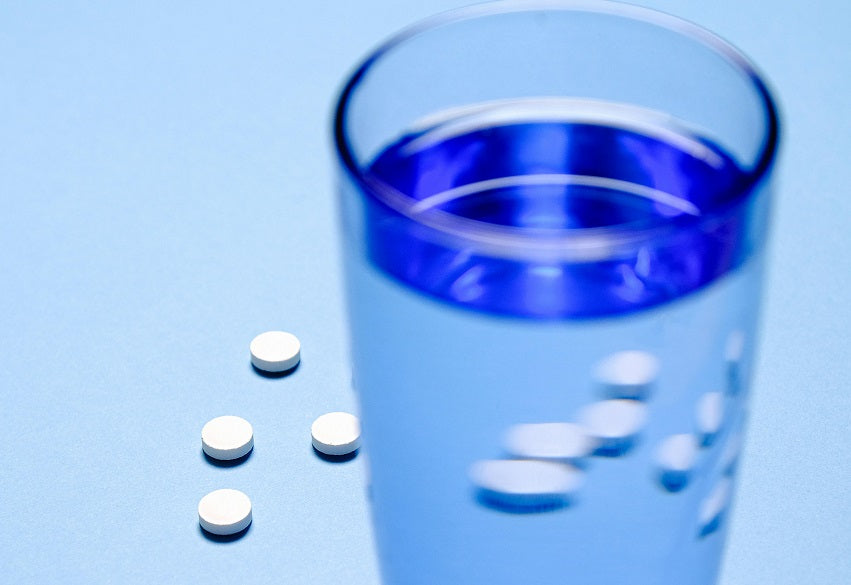 White pills on a blue surface next to a glass of water.