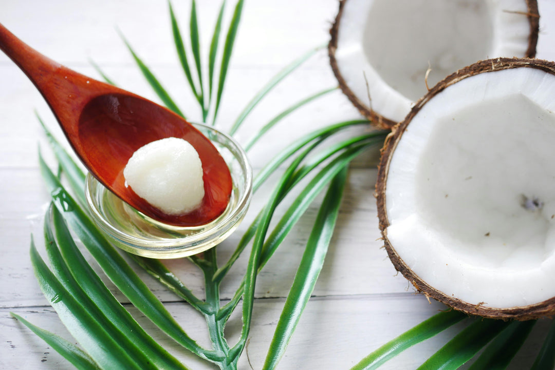 A wooden spoon holds white coconut oil over a small bowl next to a halved coconut.