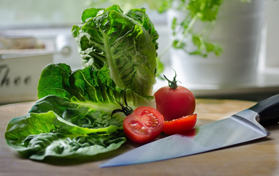 Fresh lettuce and tomatoes on a cutting board with a knife.