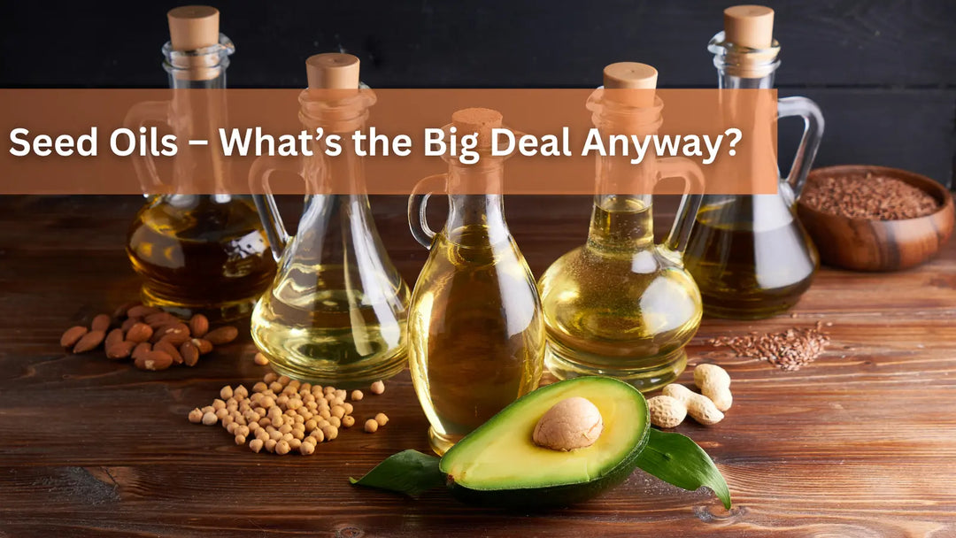 Five glass bottles of seed oils, an avocado half, and nuts on a wooden table.