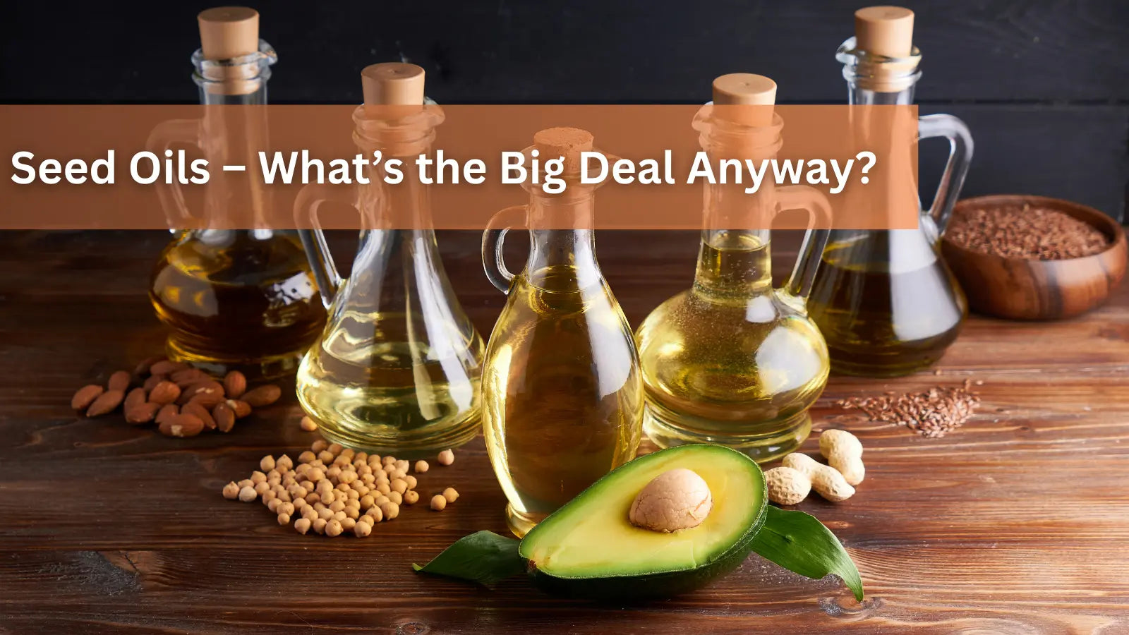 Five glass bottles of seed oils, an avocado half, and nuts on a wooden table.
