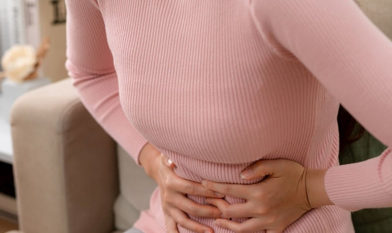 A woman in a pink sweater holding her stomach in pain.